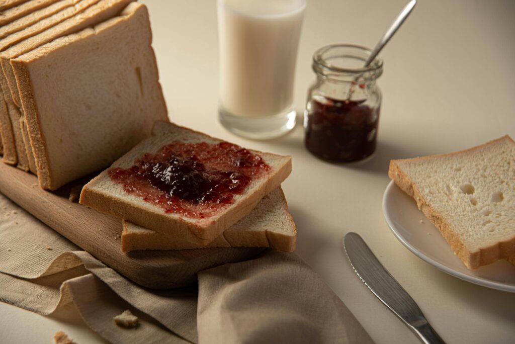 A close-up of sliced bread with strawberry jam and a glass of milk, perfect for breakfast ideas.
